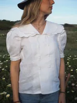 Blusa blanca de lino, de manga corta, con cuello marinero amplio decorado con estampado azul.