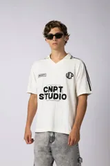 Remera tipo chomba de tejido de punto color blanco, con cuello polo y diseño de rayas verticales sutiles. Presenta estampado gráfico frontal con texto y logo, además de detalles de rayas negras en los hombros.