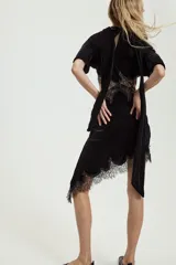 Vestido midi de terciopelo negro con cuello redondo y pañuelo integrado en el mismo tejido. Presenta mangas cortas, aberturas laterales con detalle de encaje a tono y bajo asimétrico con terminación en encaje.