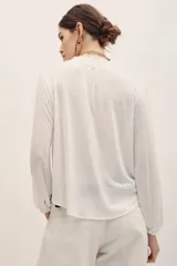 Camisa de manga larga blanca con detalles de encaje y entredos verticales, escote en V y cuello mao con volados sutiles.