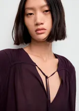 Blusa de viscosa color bordó, con escote en V y cierre de lazo, de manga larga con puños abotonados y diseño recto.