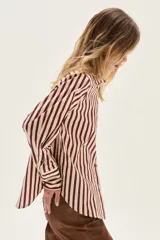 Camisa de manga larga con cuello y puños, confeccionada en tejido de rayas verticales en tonos crema y bordó. Presenta un bolsillo de parche en el pecho con un bordado exclusivo.