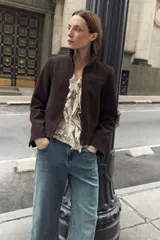 Chaqueta de cuero color marrón oscuro, con cuello alto, cierre frontal y diseño minimalista de corte recto.