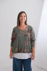 Sweater de punto amplio con diseño de flores estampadas en tonos verdes y rojizos, escote en V y mangas largas. Presenta un diseño de doble capa con un borde inferior en color blanco.