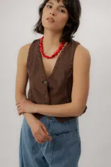 Chaleco de denim azul con cuello en V, cierre frontal con botones metálicos y pespuntes en contraste.