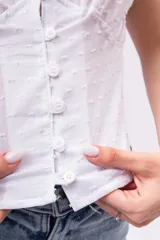 Blusa de lino liviano color blanco con textura plumeti, escote en V con detalle de encaje, botones frontales y mangas cortas.