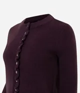 Cardigan de punto color bordó con cuello redondo, cierre frontal de botones de nácar y detalle de volados en la tapeta de botones y el ruedo. Presenta mangas largas con puños ajustados.