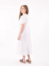 Vestido midi de broderie color blanco, con cuello mao y escote en V, cierre frontal con botones, mangas cortas abullonadas y detalle de volado en el ruedo.