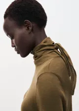 Sweater de punto fino color verde oliva, con cuello alto y detalle de lazo anudado en el frente. Presenta un diseño recto de manga larga.