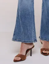 Jean wide leg de tiro medio, color azul claro, confeccionado en denim de algodón con un toque de elastano. Cuenta con cinco bolsillos, presillas para cinturón y cierre frontal con botón. El diseño destaca por su pretina regulable con cruce y broches metálicos.