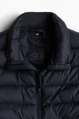 Chaleco acolchado negro con cuello alto, cierre frontal con cremallera y bolsillos laterales con cremallera.
