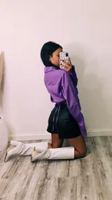 Camisa cropped negra con cuello clásico, mangas largas con puños abotonados y cierre frontal con botones. Presenta detalle de tachas plateadas en el cuello.