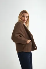 Campera corta de paño color negro, con cuello redondo, mangas largas y cierre frontal con botones a presión metálicos.