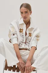 Camisa blanca de lino con bordados florales en tonos dorados y marrones en el frente y las mangas.