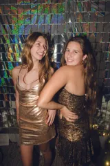 Vestido corto de fiesta color plateado con acabado brillante. Presenta un diseño de dos piezas que simula un conjunto de top y pollera, con aberturas laterales en la cintura, escote en V y tirantes finos que se cruzan en la espalda.