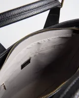 Cartera tipo tote XL Extra Large modelo Fausta, de símil cuero con textura granulada color negro. Cuenta con dos asas de mano, correa bandolera regulable y desmontable, herrajes de metal dorado envejecido y cierre superior. Presenta costura central decorativa y parche con logo en relieve en el frente.