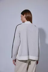 Saco de punto acanalado en color gris claro, con cierre frontal de botones oscuros. Presenta un diseño de bloques de color en las mangas, combinando negro y marrón, y un cuello redondo.