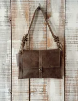 Cartera de cuero color marrón con diseño rectangular, solapa frontal con cierre de hebilla metálica y correa ajustable con detalle de nudos decorativos en los extremos.