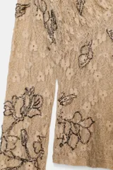 Top de manga larga con escote en pico, confeccionado en tejido de encaje con bordados florales y aplicación de abalorios decorativos.