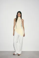 Top halter negro de tela satinada, con cuello drapeado y bajo asimétrico con caída.