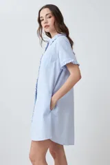 Vestido camisero corto color celeste melange, con cuello camisero y volados en el cuello, la tapeta de botones y los puños de las mangas cortas. Tiene un bolsillo de parche en el pecho.