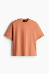 Remera de manga corta color terracota, confeccionada en punto de algodón pesado, con cuello redondo ribeteado y hombros caídos. Presenta un corte holgado.