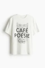 Remera blanca de manga corta y cuello redondo, con estampado gráfico en negro que simula la fachada de un café parisino con el texto "CAFÉ POÉSIE" y la dirección "Rue La Fayette, 3 Paris, France".