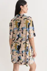 Vestido camisero corto con estampado abstracto en tonos beige, azul, negro y amarillo. Confeccionado en lino y seda, con cuello camisero, mangas cortas y cierre frontal con botones.