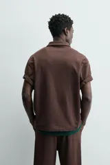 Polo de hombre de corte relajado, color marrón oscuro, confeccionado en tejido texturizado con rayas verticales. Posee cuello solapa y cierre frontal con botonadura oculta por solapa.