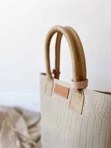 Bolso matero verde con textura croco y detalles en beige. Tiene doble asa corta y accesorio metálico en forma de cruz.