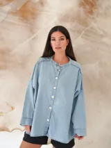 Camisa de denim liviano con lavado azul, cuello mao, manga larga y cierre frontal con botones de nácar. Presenta un corte holgado y oversize con ruedo redondeado.