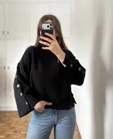 Sweater de bremer color negro con cuello alto, diseño holgado y mangas anchas con detalle de botones laterales.