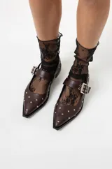 Chatas de cuero negro con punta fina, diseño destalonado y tira con hebilla metálica plateada. Presentan apliques de tachas plateadas en toda la superficie.