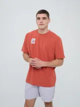 Remera de manga corta color beige, con cuello redondo y diseño holgado. Cuenta con un pequeño estampado rectangular en el pecho con motivo futbolero.