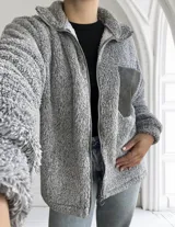 Campera gris de tela tipo peluche con cierre frontal y bolsillo de cuero sintético en el pecho.