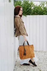 Bolso tipo tote de cuero gamuzado en color marrón, con textura grabada tipo cocodrilo, manijas de cuero oscuro y detalle de borla colgante.