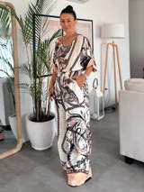 Blusa de satén con estampado de cadenas y hojas en tonos blanco, marrón y negro. Tiene corte amplio, mangas cortas y cuello redondo. Se ajusta a la cintura con un cinturón elástico negro con hebilla dorada.