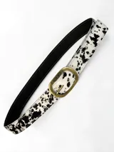 Cinto de cuero de pelo con estampado animal print tipo vaca en color blanco y negro, con hebilla metálica ovalada en tono bronce viejo con la marca grabada.