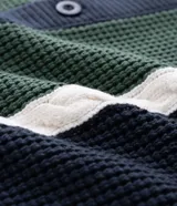 Cardigan masculino de punto con cuello camisero y cierre frontal de botones. Presenta un diseño con paneles frontales en color verde y blanco que contrastan con el cuerpo azul marino, destacando por su textura de tejido diferenciada.
