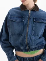 Campera bomber de denim azul con cierre frontal, cuello de pana en color marrón y bolsillos frontales con solapa. Presenta un diseño corto con cintura elástica.