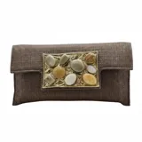 Bolso tipo sobre color dorado, confeccionado en yute de algodón con acabado texturizado y un llamativo aplique central metálico rectangular con piedras de resina en tonos tierra y gris. Incluye asa de cadena para llevar al hombro.