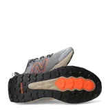 Championes de trail running New Balance modelo Garoe, color gris con detalles en naranja y suela en tono arena. Presentan tecnología Fresh Foam en la entresuela para mayor amortiguación y refuerzos en la puntera para mayor protección.