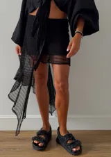 Falda corta negra de encaje con diseño irregular y un volante largo asimétrico en un lateral. Posee cintura elástica y forro interior.