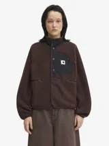 Campera de polar estilo sherpa en color marrón oscuro, con cuello alto, cierre frontal con botones a presión y bolsillo en el pecho con solapa de nylon negro y logo de la marca. Cuenta con bolsillos laterales con cierre y puños elásticos.