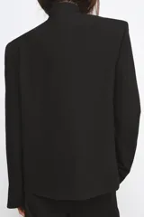 Blazer de cuello alto y manga larga con cierre frontal de botones metálicos en relieve. Presenta aberturas en los puños con botones y falsos bolsillos de vivo en el delantero.