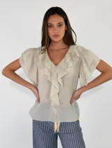 Blusa de manga corta color beige, con escote en V y volados que bordean el cuello y la parte delantera.