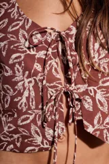 Chaleco marrón con estampado de hojas blancas, escote en V y lazos ajustables en el frente.
