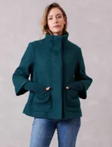 Tapado de tejido boucle color verde petróleo, con silueta evasé y largo a la cadera. Presenta cuello alto envolvente, cierre frontal oculto con botones a presión y bolsillos frontales de gran tamaño. Posee mangas 3/4 de corte amplio con puños de tejido rib al tono que se extienden para cubrir las muñecas.