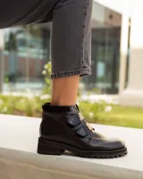 Bota corta de cuero color negro, estilo botín, con suela track gruesa y dos tiras ajustables con hebillas brillantes en el empeine.