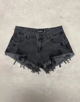 Short de denim negro de tiro medio, con roturas marcadas en la parte delantera y terminaciones deshilachadas en el ruedo. Cuenta con bolsillos clásicos y cierre frontal de botón y cremallera.